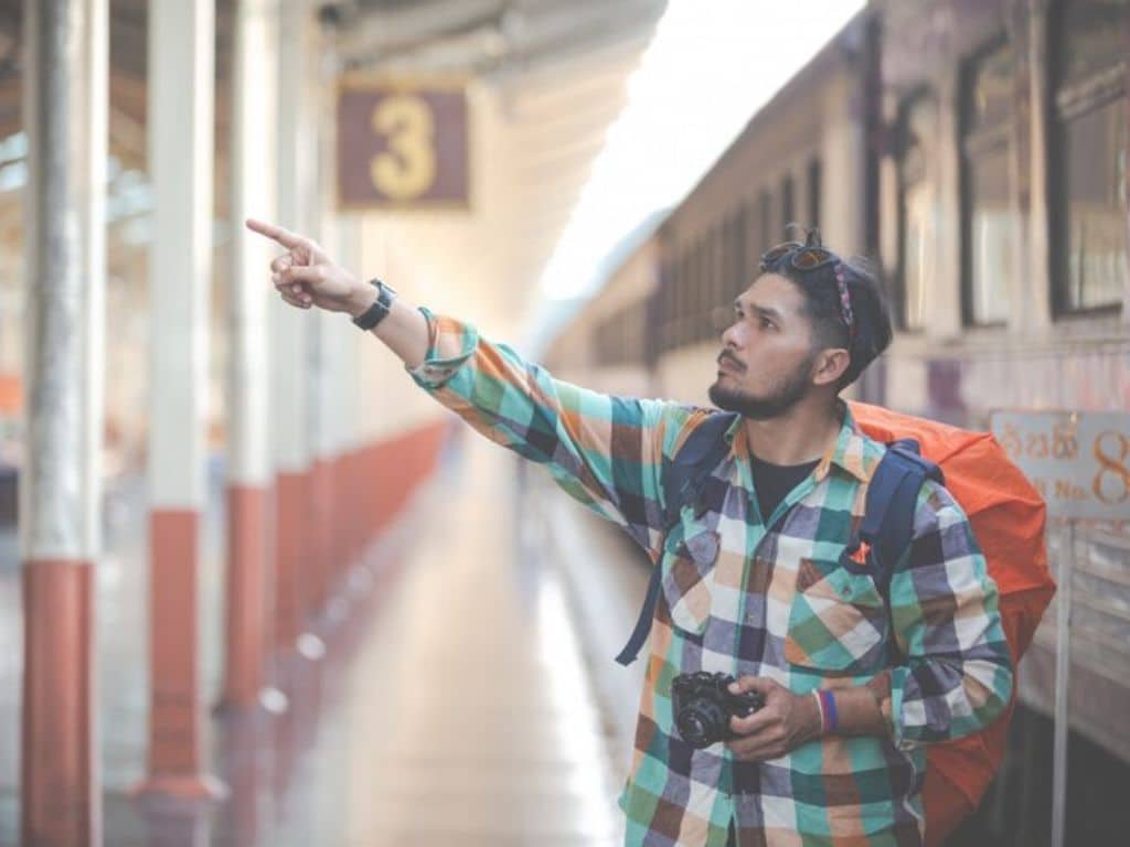 Young traveler with backpack and camera pointing at train station platform in Gujarat