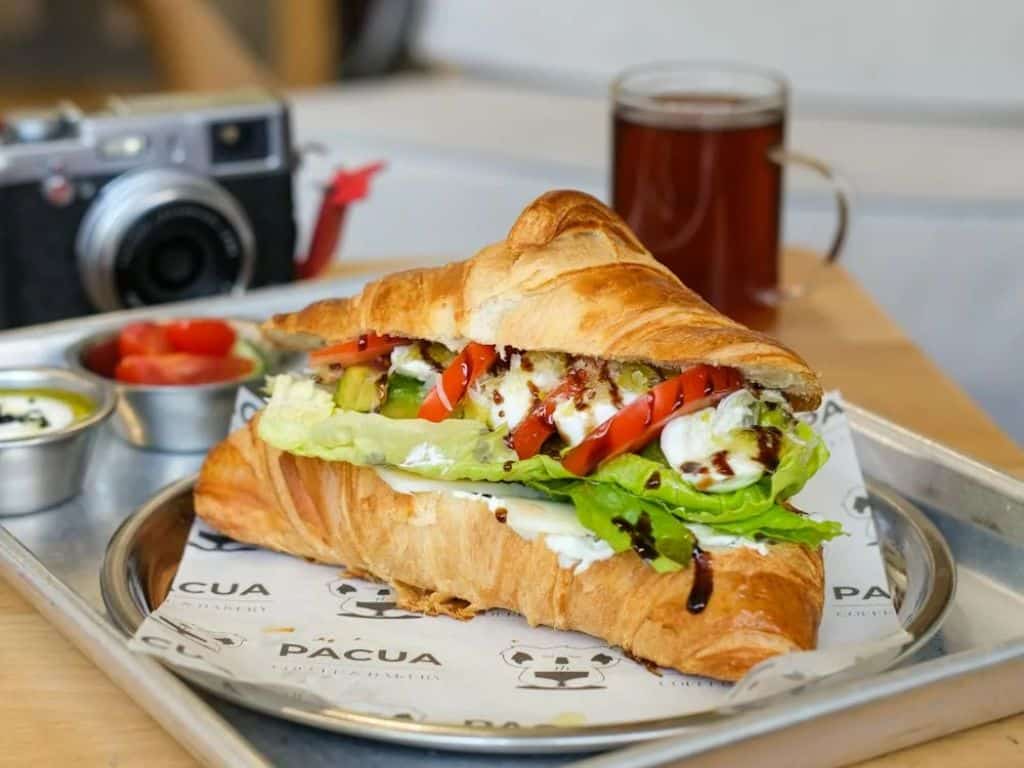Fresh croissant sandwich with vegetables and coffee in a cozy café setting.