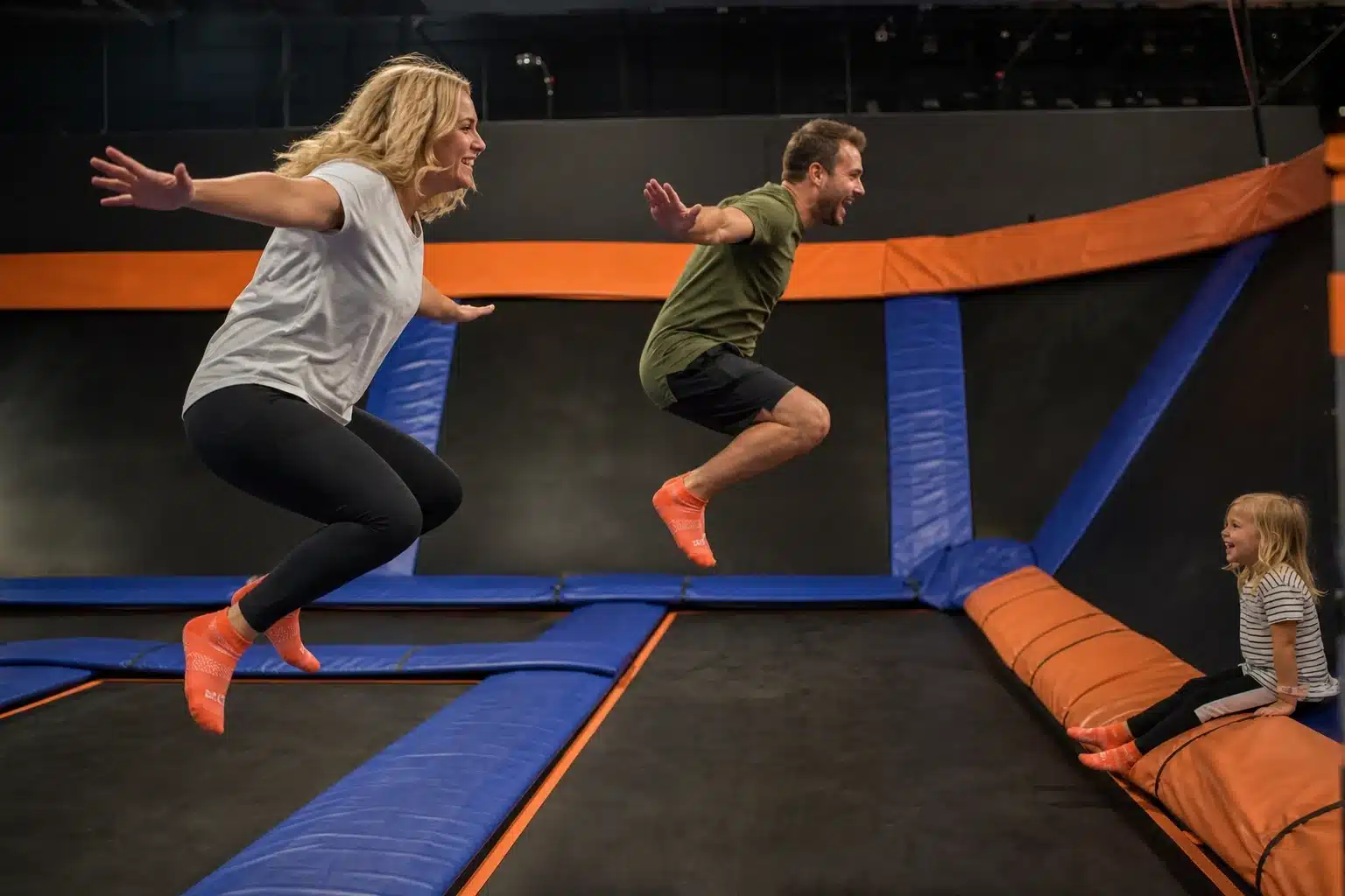 Parents bouncing together on trampolines while their child plays nearby.